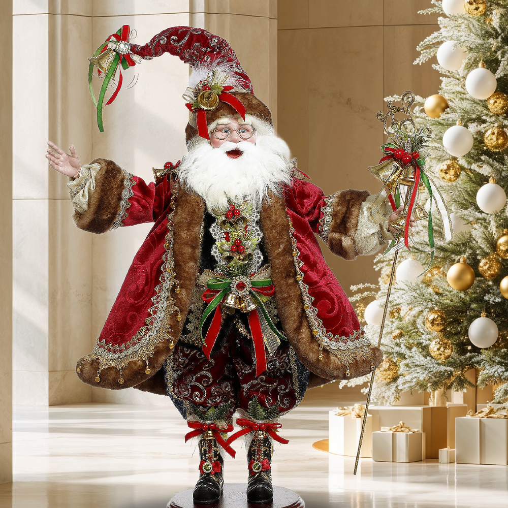 Mark Roberts collectible Santa in red velvet and fur-trimmed coat with gold and green embellishments beside a Christmas tree.